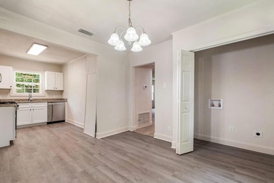 Kitchen featuring appliances with stainless steel finishes, light wood-type flooring, white cabinets, a chandelier, and ornamental molding
