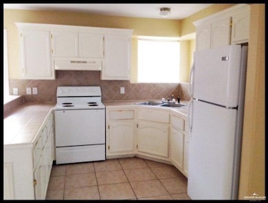 Kitchen with white appliances, tile countertops, a sink, under cabinet range hood, and light tile patterned flooring