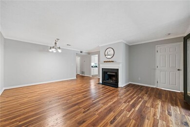 Unfurnished living room with a chandelier, wood finished floors, baseboards, a fireplace with flush hearth, and ornamental molding