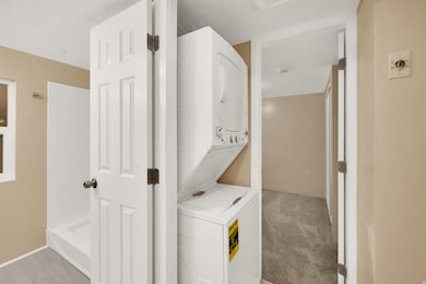 Laundry room with stacked washer / drying machine and light carpet