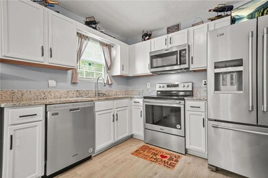 Kitchen featuring appliances with stainless steel finishes, light wood-style flooring, white cabinets, light stone counters, and a textured ceiling