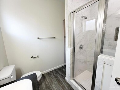 Full bath featuring wood tiled floor, a marble finish shower, toilet, and baseboards