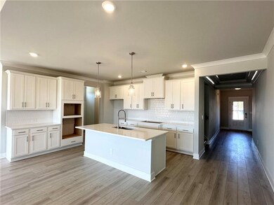 Kitchen featuring backsplash, a center island with sink, decorative light fixtures, light wood finished floors, and white cabinetry