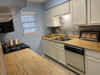 Kitchen featuring light countertops, a textured wall, white dishwasher, light tile patterned flooring, and tasteful backsplash