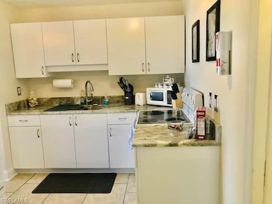 Kitchen featuring white microwave, white cabinets, a sink, electric stove, and light tile patterned floors