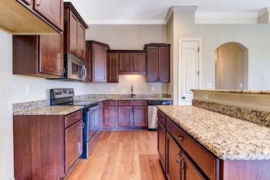 Kitchen featuring stainless steel appliances, light stone countertops, light wood-style floors, crown molding, and dark brown cabinetry