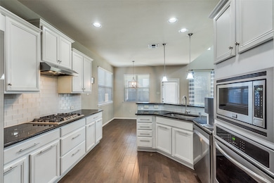 Kitchen with appliances with stainless steel finishes, white cabinets, hanging light fixtures, decorative backsplash, and recessed lighting