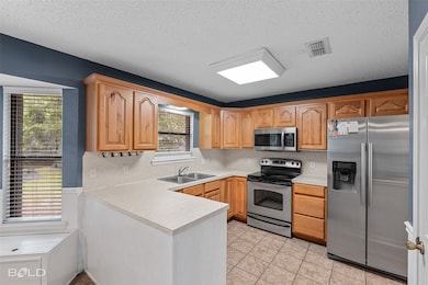 Kitchen featuring appliances with stainless steel finishes, light countertops, a textured ceiling, light tile patterned floors, and backsplash