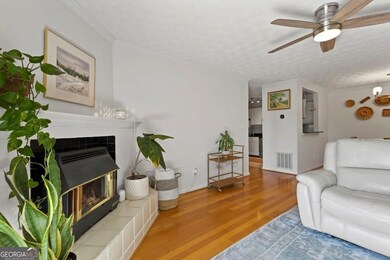 Living room featuring wood finished floors, visible vents, ornamental molding, baseboards, and ceiling fan