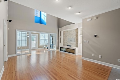 Unfurnished living room featuring a glass covered fireplace, baseboards, wood finished floors, and a textured ceiling