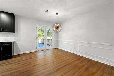 Unfurnished dining area with french doors, wood finished floors, a chandelier, a wainscoted wall, and baseboards