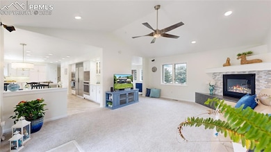 Living area with ceiling fan, a stone fireplace, vaulted ceiling, light carpet, and recessed lighting
