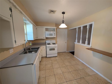 Kitchen featuring white cabinets, white appliances, hanging light fixtures, light tile patterned flooring, and light countertops
