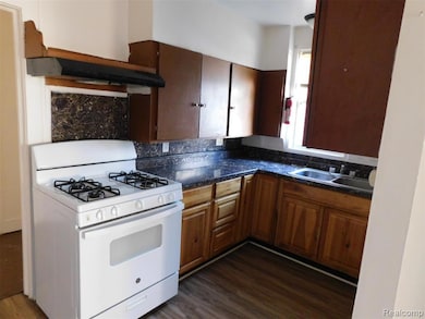 Kitchen with white range with gas stovetop, dark wood finished floors, backsplash, and under cabinet range hood