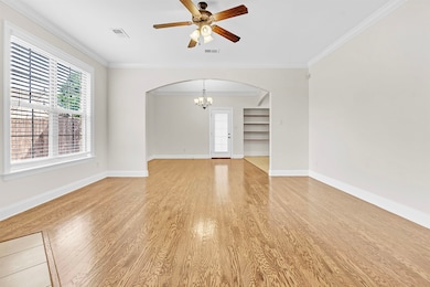Empty room with arched walkways, light wood-style floors, a chandelier, a ceiling fan, and crown molding