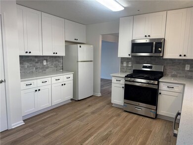 Kitchen with stainless steel appliances, white cabinets, light wood-style floors, and light stone countertops