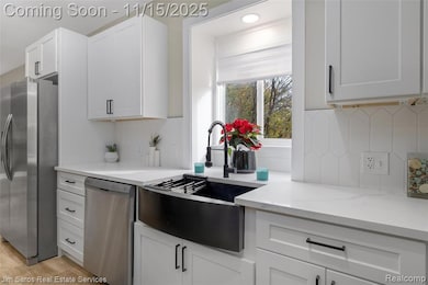Kitchen with appliances with stainless steel finishes, white cabinets, light wood-type flooring, light stone counters, and decorative backsplash