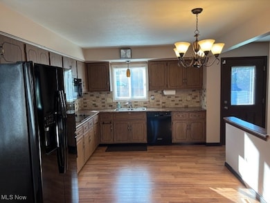 Kitchen with black appliances, hanging light fixtures, tasteful backsplash, and light wood-style flooring