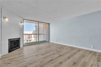 Unfurnished living room featuring a wall of windows, a textured ceiling, wood finished floors, and a fireplace