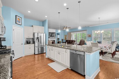 Kitchen with stainless steel appliances, light wood-style floors, a chandelier, open floor plan, and a center island with sink