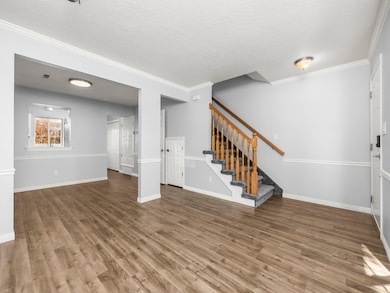 Unfurnished living room featuring ornamental molding, wood finished floors, a textured ceiling, and stairway