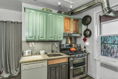 Kitchen featuring range with two ovens, backsplash, white dishwasher, radiator, and light stone countertops