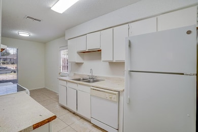 Kitchen featuring white appliances, a textured ceiling, light countertops, white cabinets, and light tile patterned floors