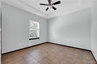 Spare room with a raised ceiling, baseboards, and ceiling fan