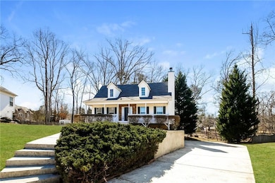 Cape cod home with a chimney, driveway, and covered porch