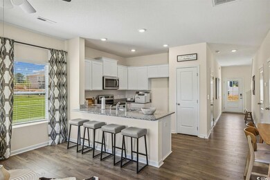 Kitchen featuring stainless steel appliances, a peninsula, white cabinets, dark wood-style flooring, and light stone counters