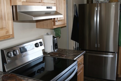 Kitchen with under cabinet range hood, dark countertops, and appliances with stainless steel finishes