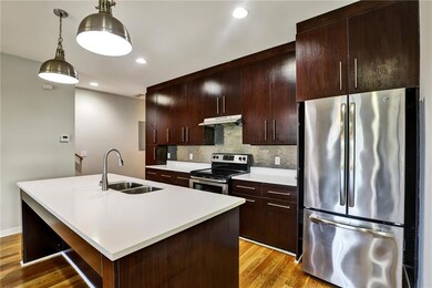 Kitchen with appliances with stainless steel finishes, light countertops, tasteful backsplash, light wood-style flooring, and a center island with sink