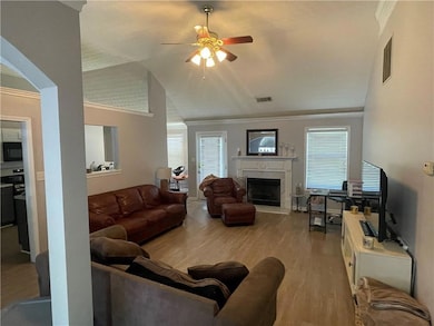 Living room with crown molding, a ceiling fan, lofted ceiling, wood-look floors, and a premium fireplace