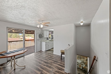 Sitting room with dark wood finished floors, a ceiling fan, a textured ceiling, and an upstairs landing