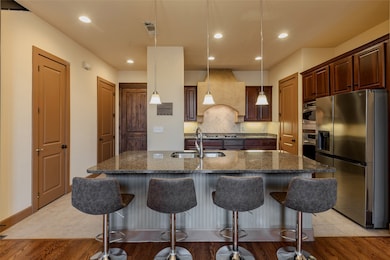 Kitchen featuring appliances with stainless steel finishes, decorative light fixtures, dark stone countertops, recessed lighting, and an island with sink