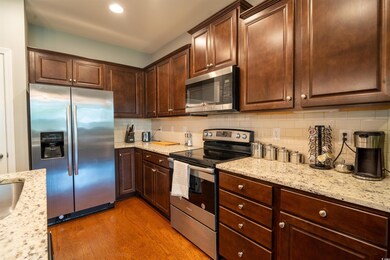 Kitchen featuring stainless steel appliances, light wood-style floors, backsplash, light stone countertops, and dark brown cabinets