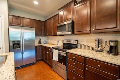 Kitchen featuring stainless steel appliances, light wood-style floors, backsplash, light stone countertops, and dark brown cabinets