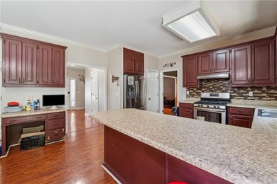 Kitchen featuring stainless steel appliances, under cabinet range hood, light countertops, dark wood-style flooring, and a peninsula