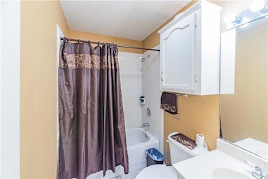Full bathroom featuring shower / bath combination with curtain, toilet, vanity, and a textured ceiling