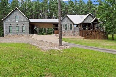 View of front of home with an attached carport, driveway, a front yard, stone siding, and view of scattered trees