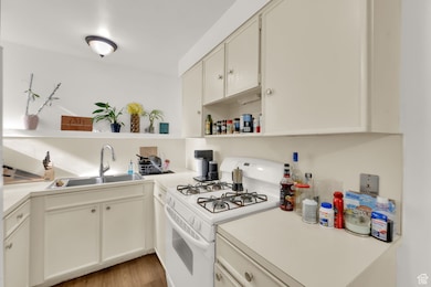 Kitchen with open shelves, white range with gas stovetop, light countertops, and light wood finished floors