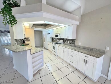 Kitchen featuring sink, light stone counters, kitchen peninsula, white appliances, and white cabinets