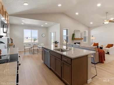 Kitchen featuring stainless steel appliances, vaulted ceiling, light wood-type flooring, a fireplace, and light stone counters