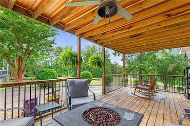 Wooden terrace with a fire pit, ceiling fan, and view of wooded area