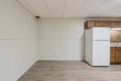 Kitchen with brown cabinetry, a paneled ceiling, freestanding refrigerator, light wood-style floors, and light countertops