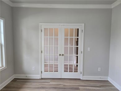 Empty room with french doors, crown molding, wood finished floors, and baseboards
