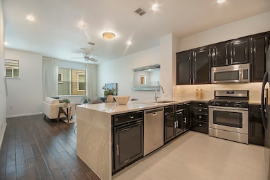 Main level kitchen with dark cabinetry, stainless steel appliances, light stone countertops, decorative backsplash, and a peninsula