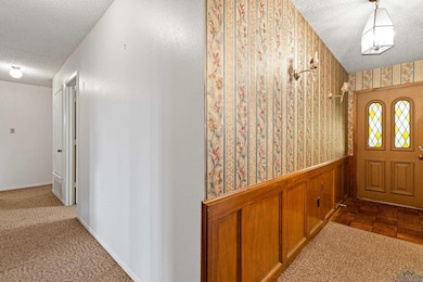 Entryway featuring a textured ceiling, wallpapered walls, and wainscoting