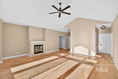 Unfurnished living room featuring light wood-style floors, a fireplace, vaulted ceiling, ceiling fan, and a chandelier