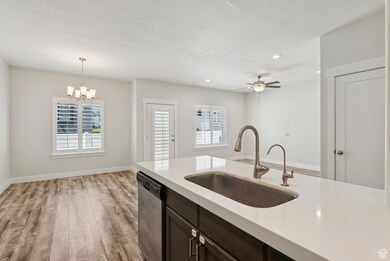 Kitchen featuring light wood-style flooring, stainless steel dishwasher, dark brown cabinets, a chandelier, and pendant lighting